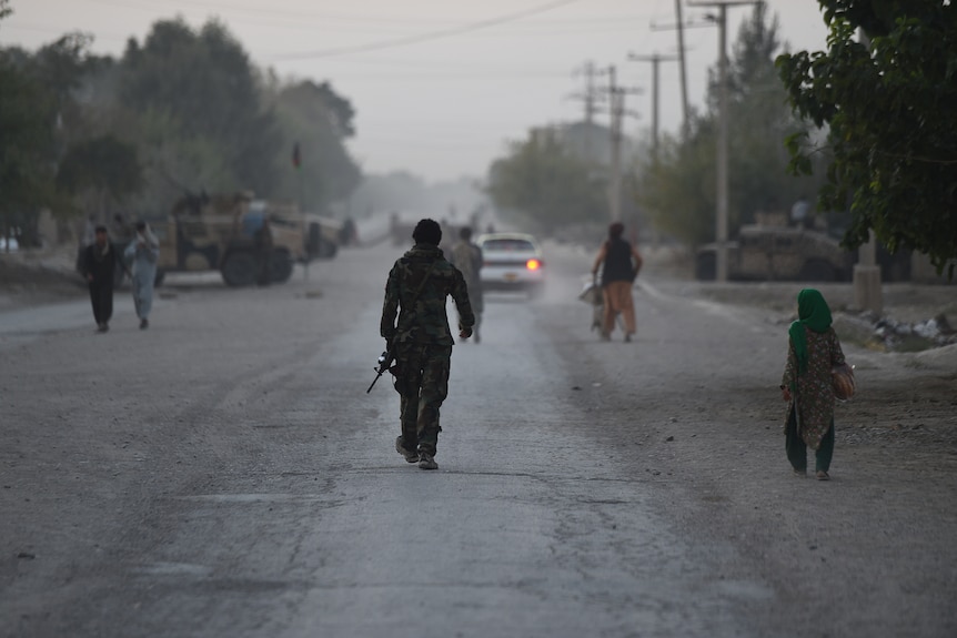 A wide dirt road can be seen, with military vehicles and figures in the distance