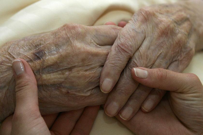 A young carer holds the hands of an elderly woman in a nursing home (Reuters)