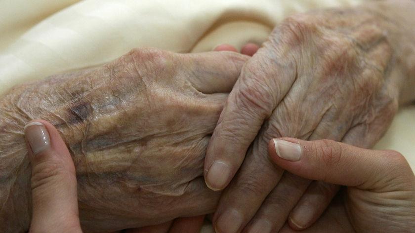 A young carer holds the hands of an elderly woman in a nursing home (Reuters)