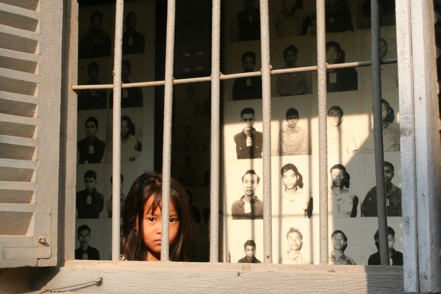 A young girl walks between grey prison bars and row of black and white mugshots.
