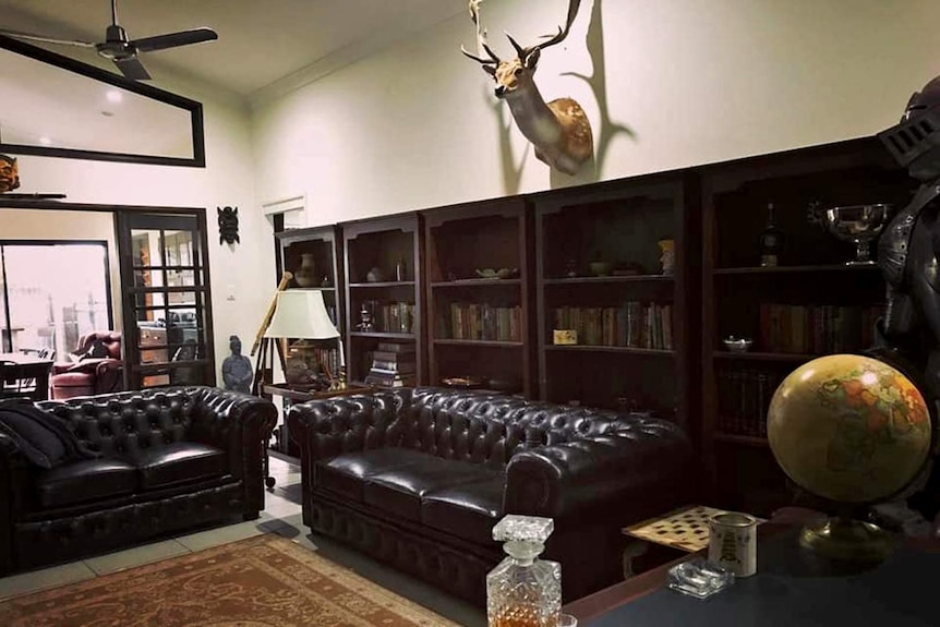 A home interior, the house has dark leather lounges, a deer head on the wall, a world globe and a whiskey bottle.