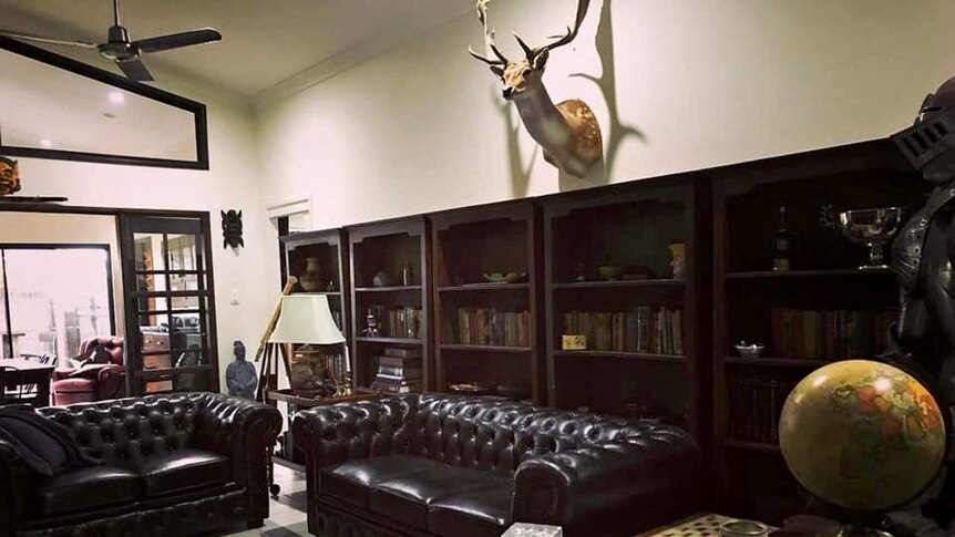 A home interior, the house has dark leather lounges, a deer head on the wall, a world globe and a whiskey bottle.