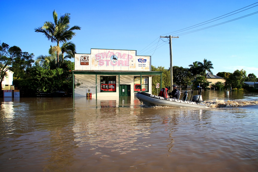 Exterior shot of a flooded-out street with a police rubber dinghy motoring past a corner store.