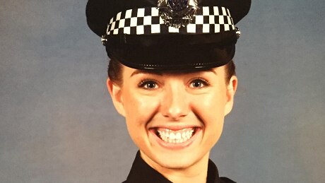 A smiling young policewoman in full uniform.