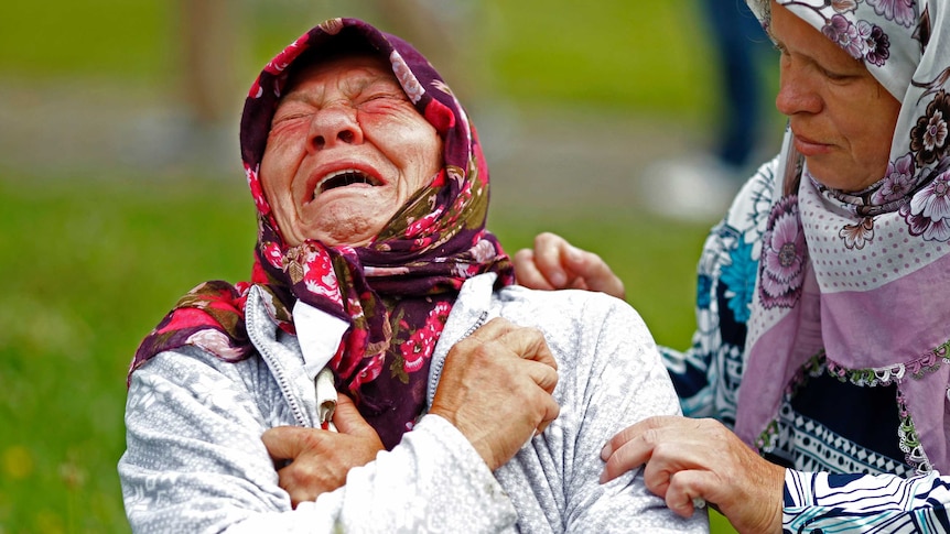 An older woman with a scarf on her head cries.