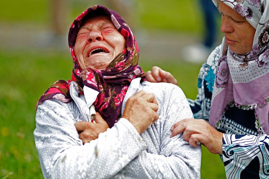 An older woman with a scarf on her head cries.