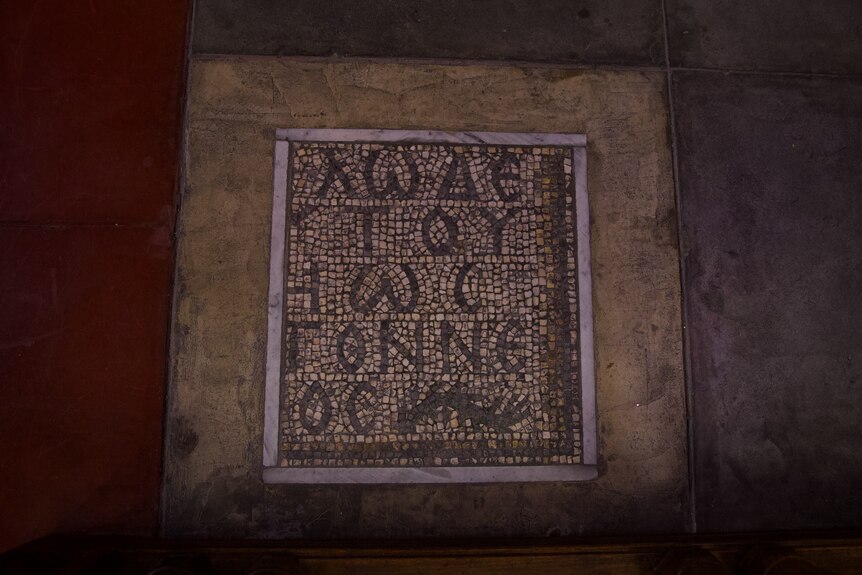 A black and white mosaic featuring ancient words on a floor