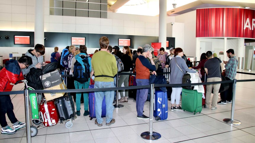 People line up with luggage in a queue at an airport.
