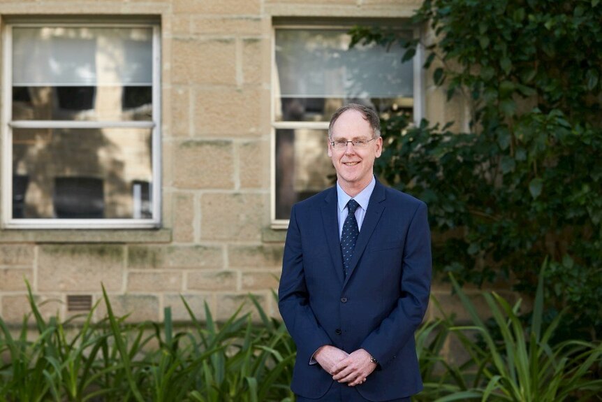 Professor Robertson stands in front of a brick wall.