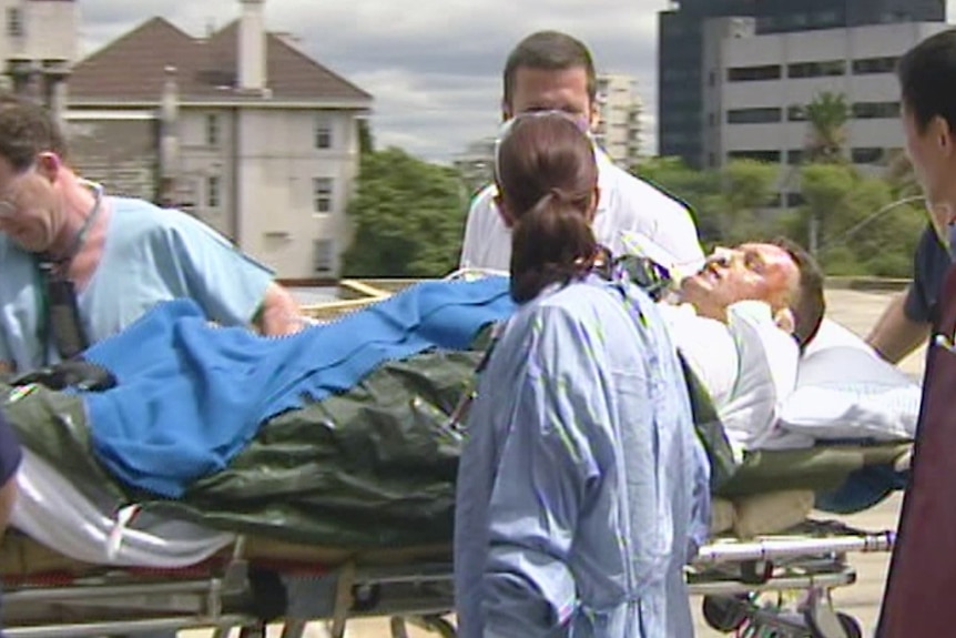 Man with severe burns on a stretcher. A team of doctors surrounds him.