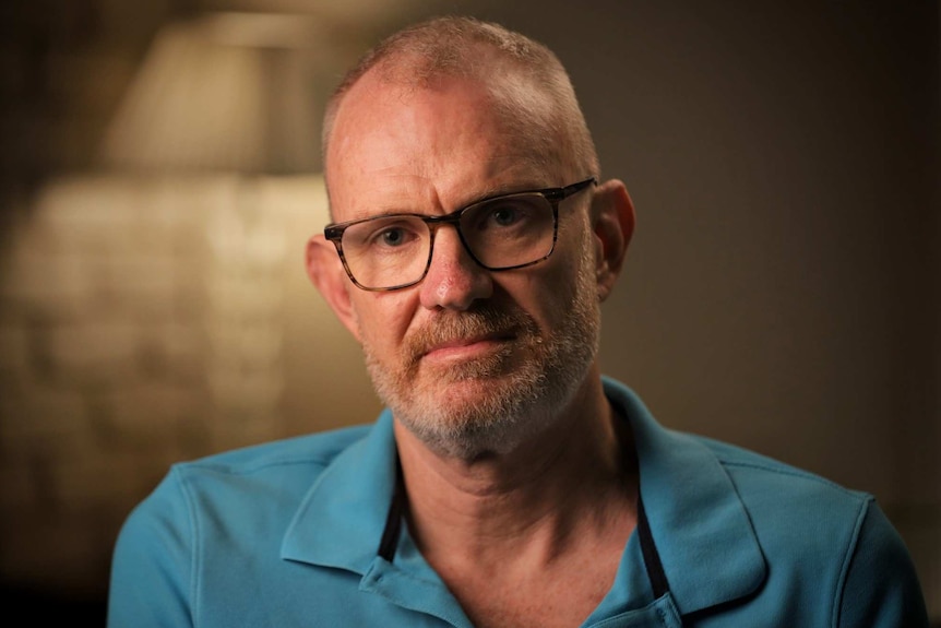 A man wears glasses and a blue collared shirt.