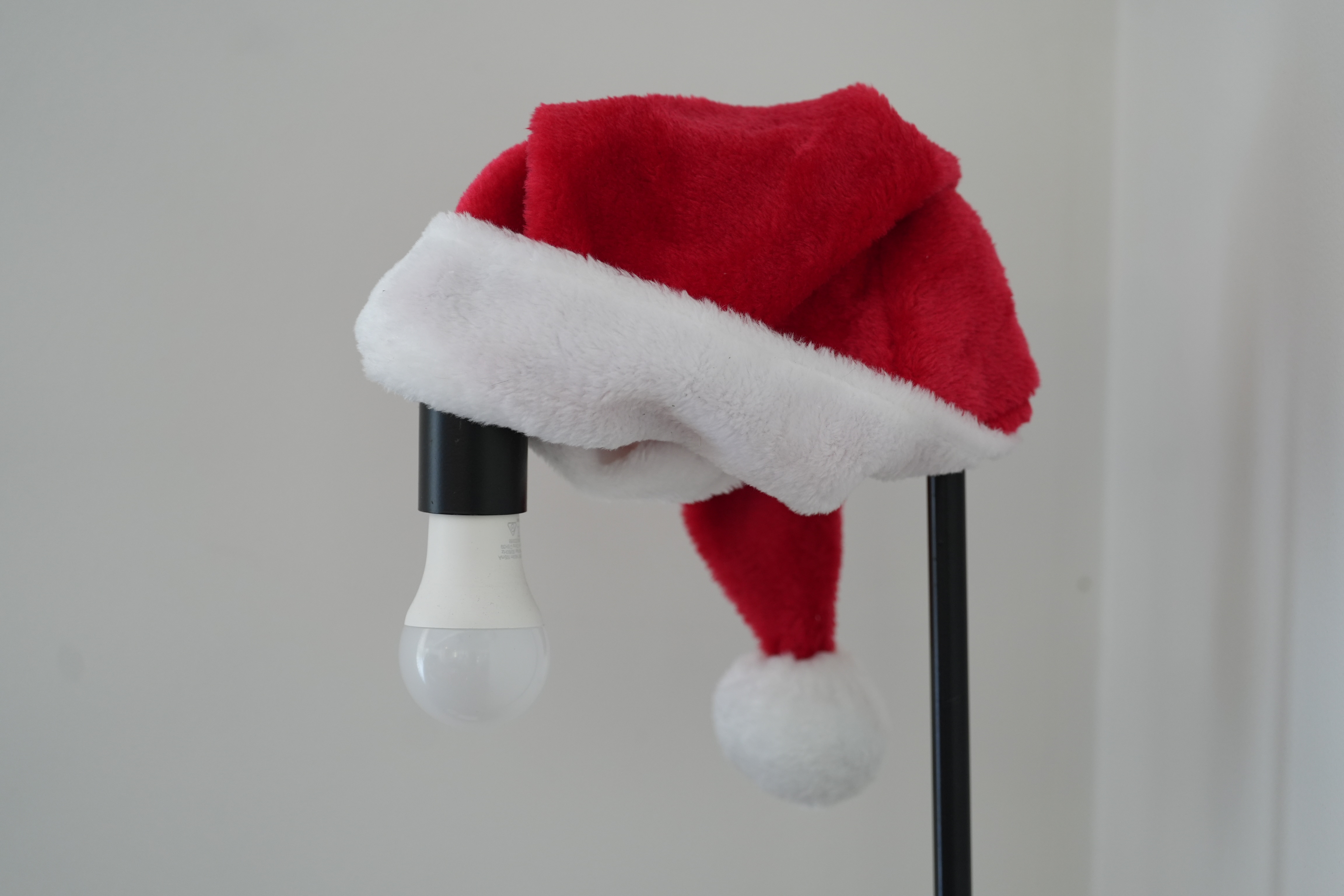 Um chapéu de Papai Noel vermelho e branco apoiado em uma lâmpada.