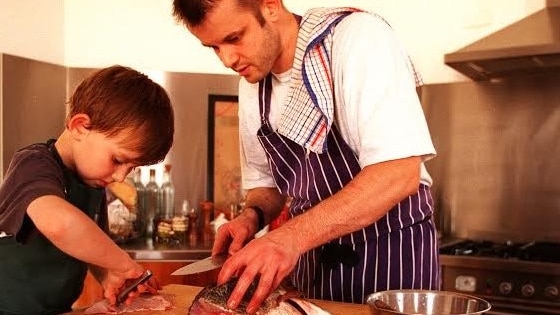 A young boy and his father carefully fillet a fish