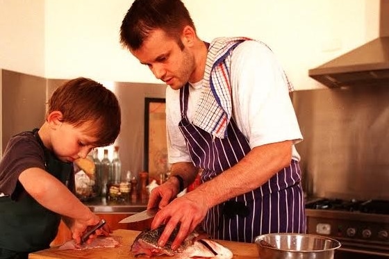 A young boy and his father carefully fillet a fish