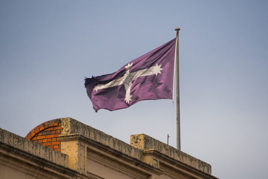 a blue eureka flag with a white cross and southern cross flies above a red brick building at dusk