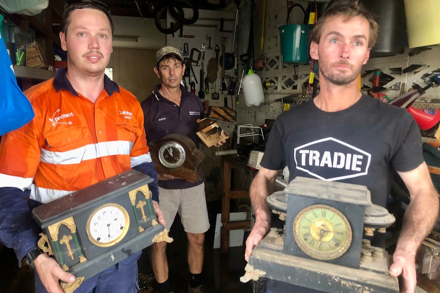 three men hold antique clocks