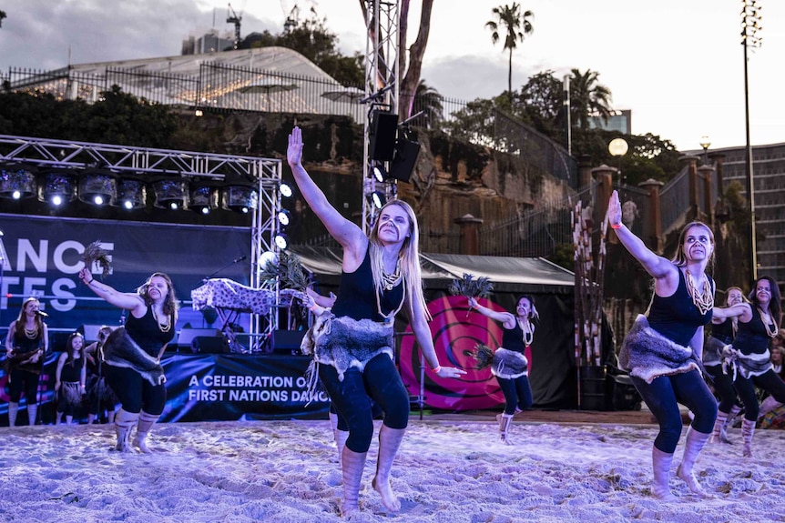 Colour photo of Djirri Djirri dance group performing in sand circle in front of stage at Dance Rites 2018.