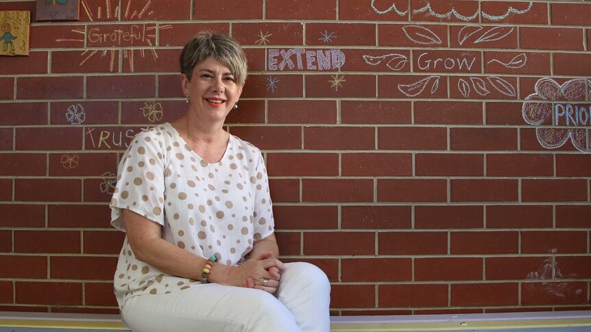 A woman sitting on a bench in front of a red brick wall with chalk words on it