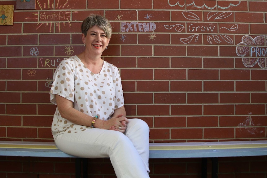 A woman sitting on a bench in front of a red brick wall with chalk words on it