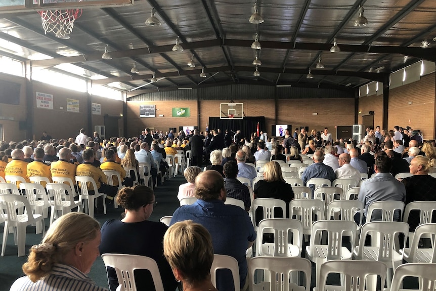Crowds of people are seated on plastic chairs inside the brick walls of the Holbrook Sports Stadium.