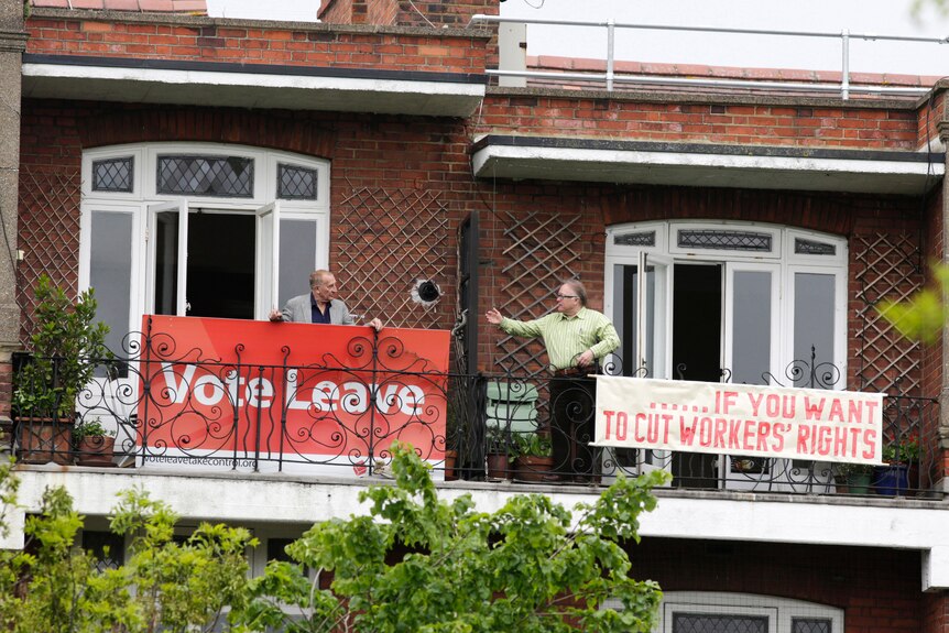 Two London neighbours hold rival Brexit signs: left reads "Vote Leave", right reads "…if you want to cut workers rights"