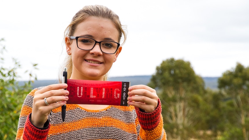 Girl in striped jumper, wearing glasses, holding a pen with a banner coming from it