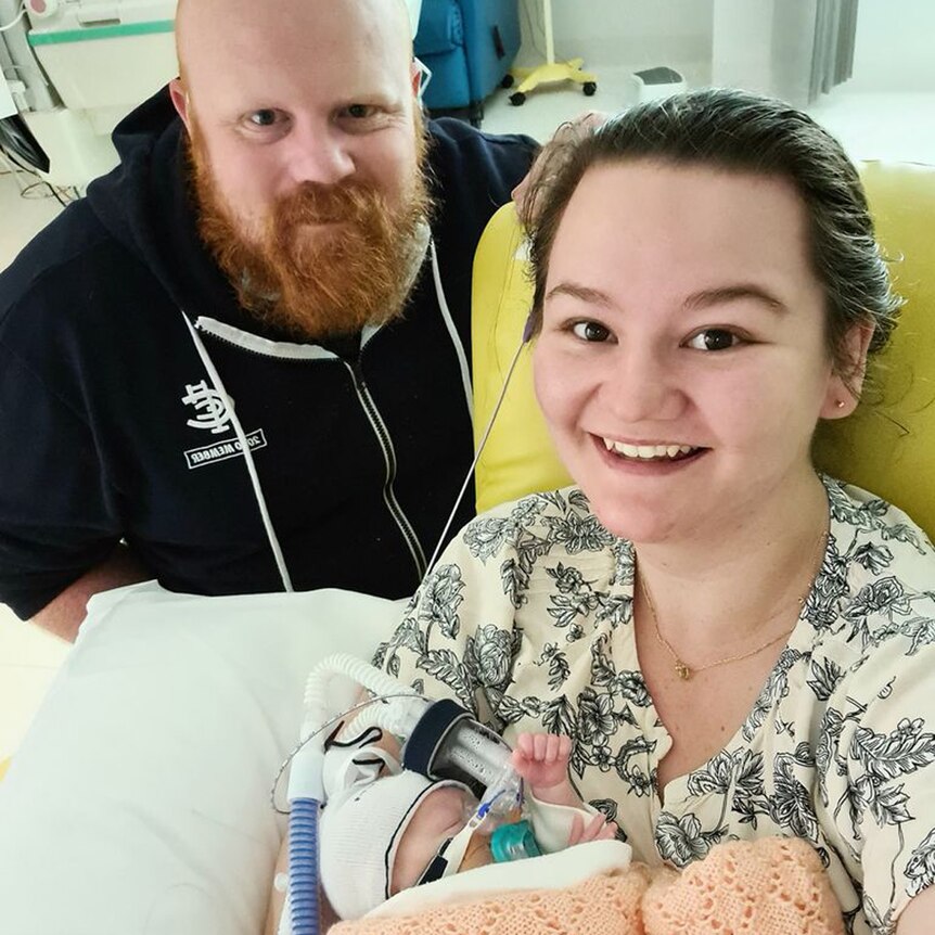 Aaron Pillar (left) leans over behind his wife Jess (right) as she nurses baby Charlotte.