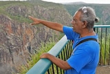 Warrgamay custodian standing at a lookout pointing over a giant gorge towards Wallaman Falls