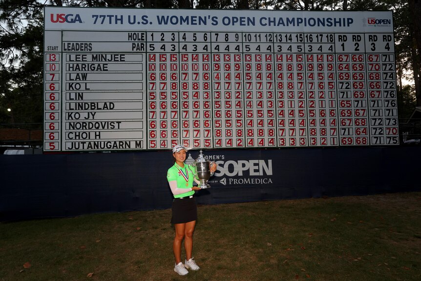 Australian golfer Minjee Lee holds the US Open trophy in front of a giant scoreboard. 