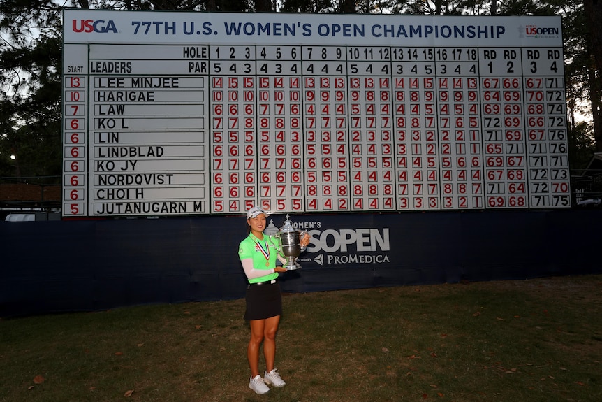 Australian golfer Minjee Lee holds the US Open trophy in front of a giant scoreboard. 