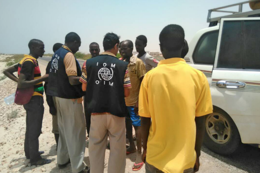 An aid worker speaks with a handful of migrants on a Yemen beach.