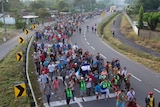 Hundreds of Central American migrants in a long caravan walk on a highway.