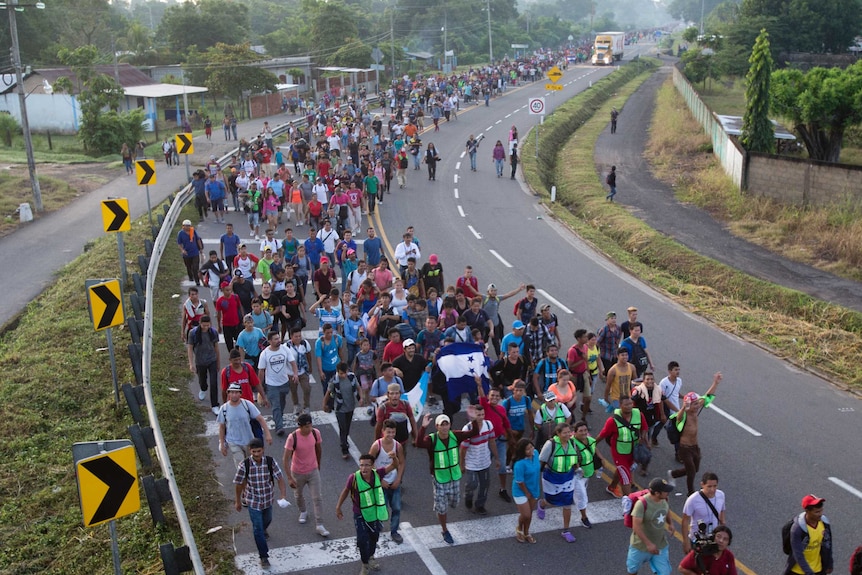 Hundreds of Central American migrants in a long caravan walk on a highway.
