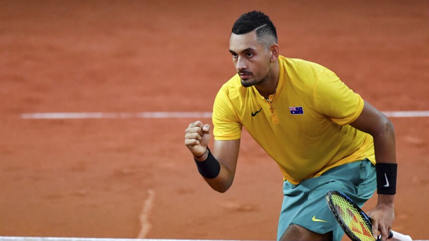Nick Kyrgios, wearing Australian colours, celebrates at the net after winning a point.