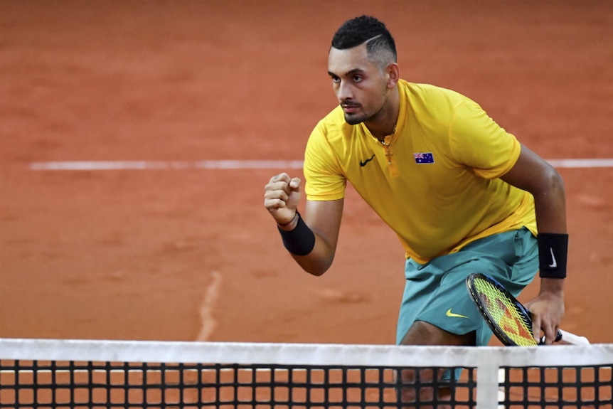 Nick Kyrgios, wearing Australian colours, celebrates at the net after winning a point.