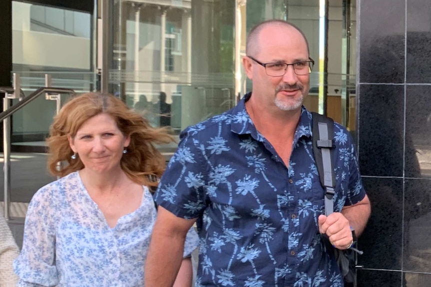 A middle-aged man and woman holding hand exit a Perth court building