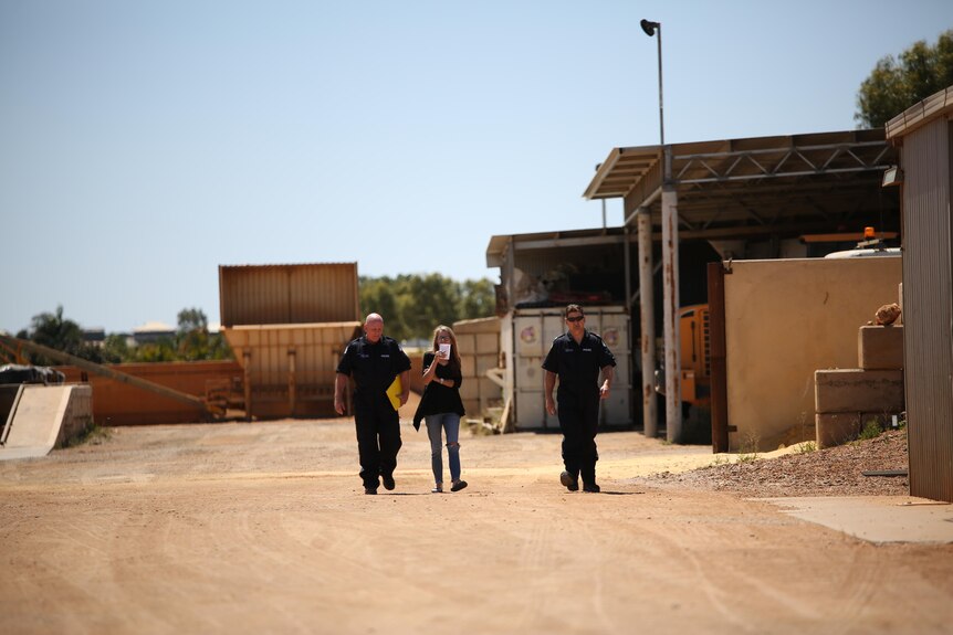 Two police walk and talk with a woman in a work yard.