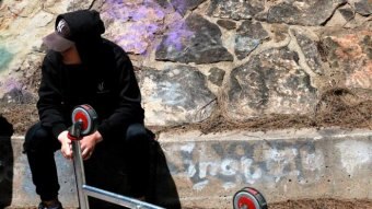 A young man in a hoodie sits near a disused shopping trolley.