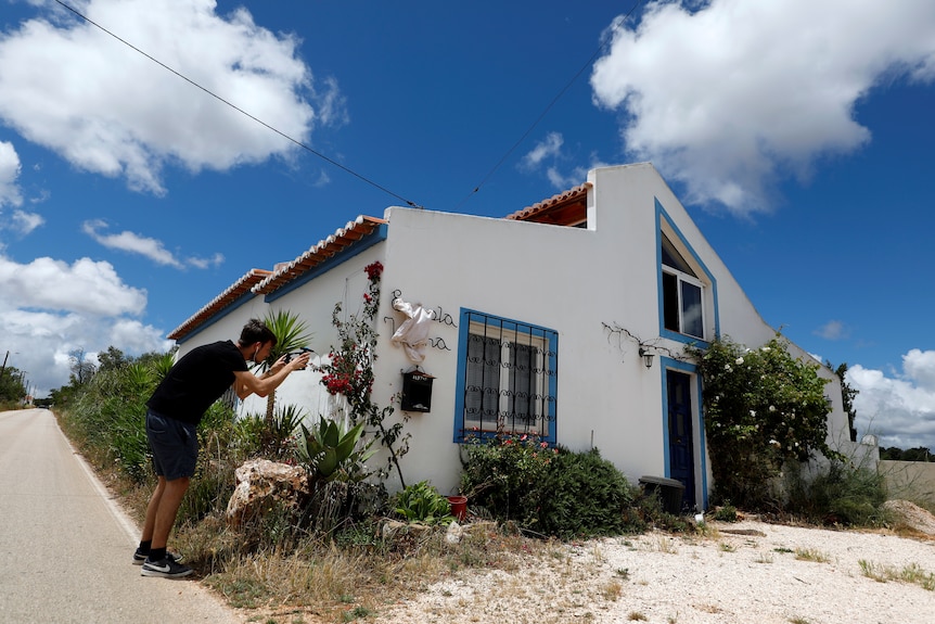 A reporter takes a photograph alongside a white-walled house in Portugal