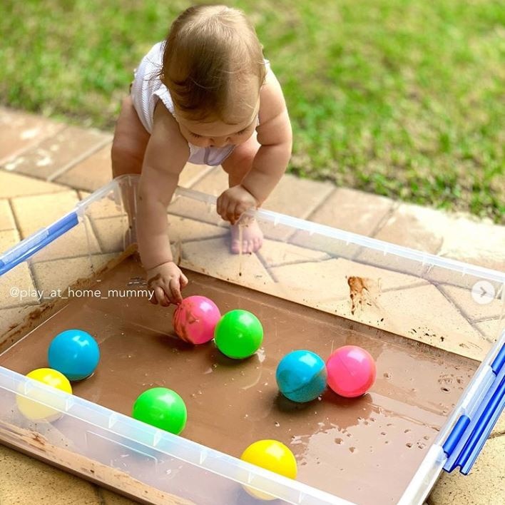 Baby playing with a home ball pit filled with edible 'mud' made of cocoa powder and flour.
