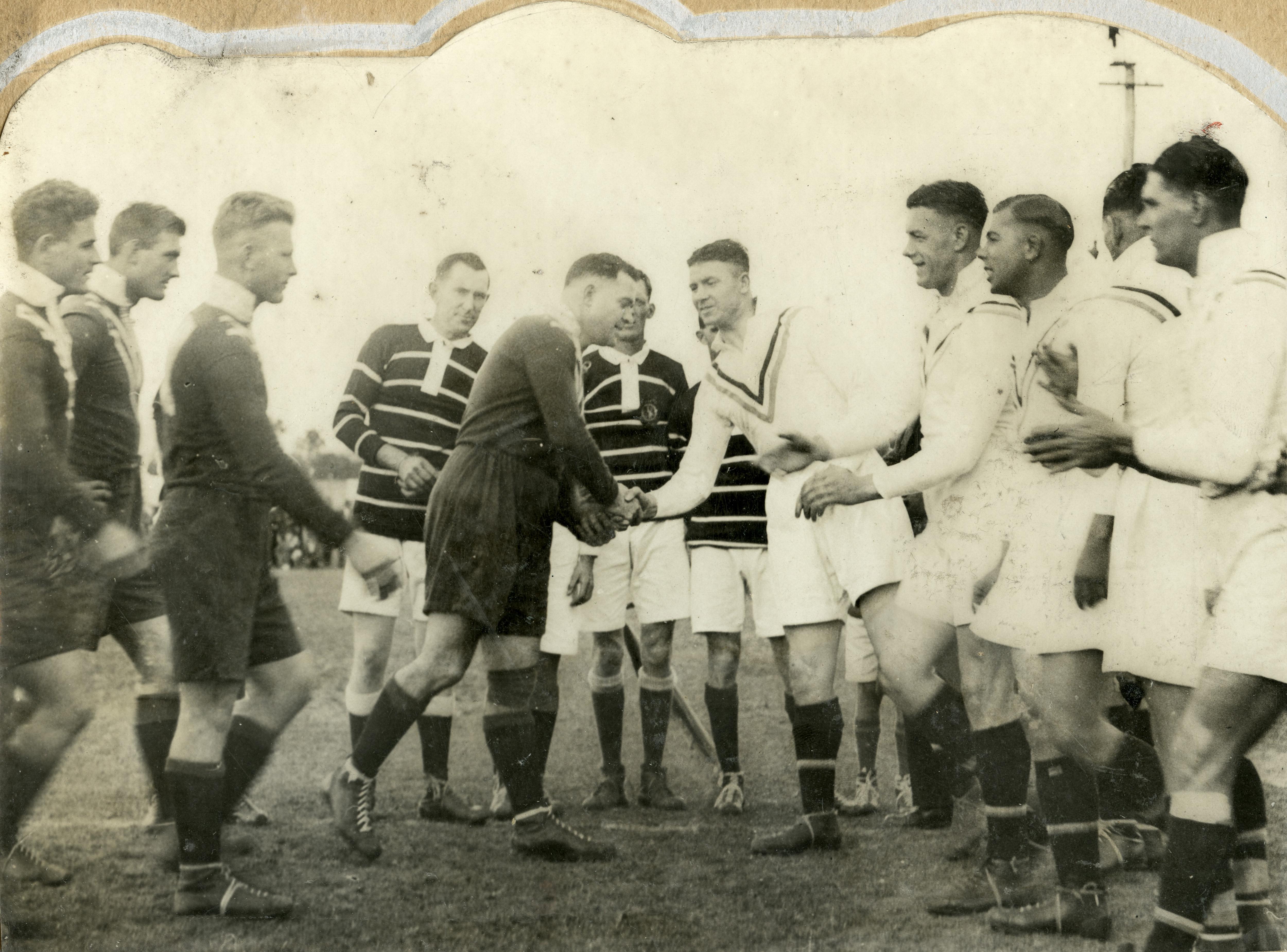 Old black and white photograph of rugby league captains shaking hands with other players around them.