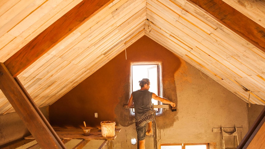 James Galletly on a ladder working painting the interior of his hay bale house.