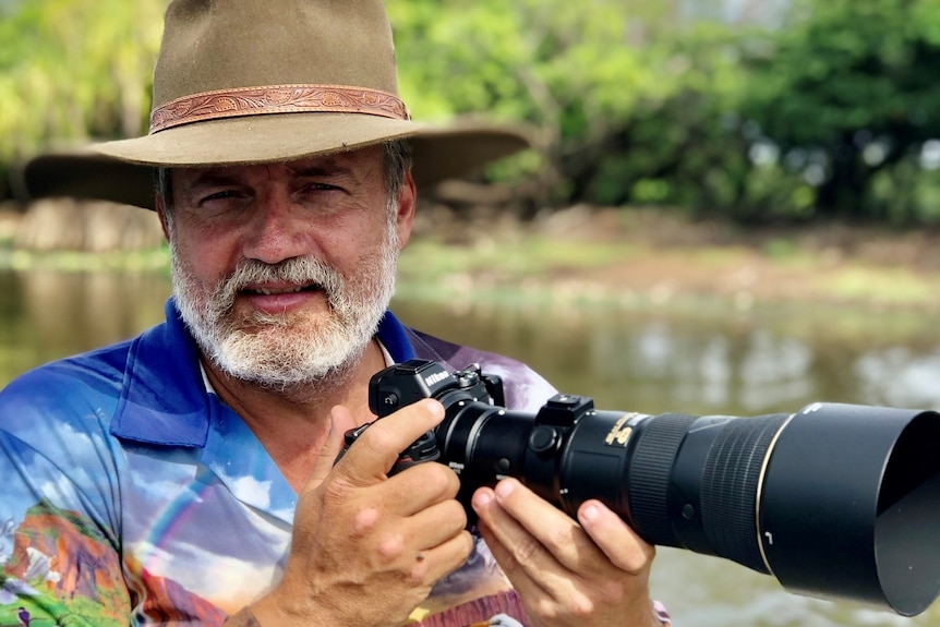 A bearded man in a hat holding a ginormous camera.