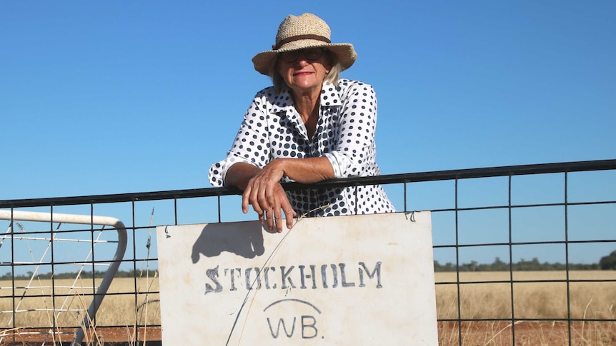 A woman wearing a hat leans over a gate with a sign reading Stockholm