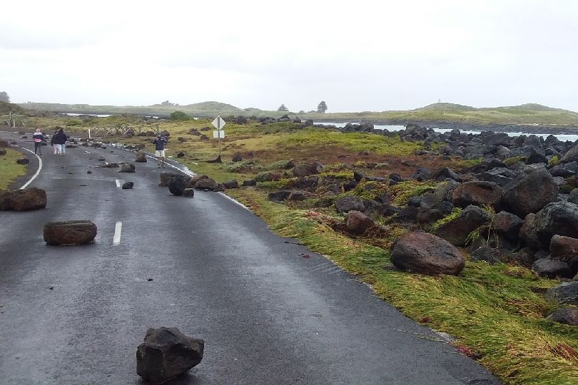 Large rocks lie across a road next to the ocean.