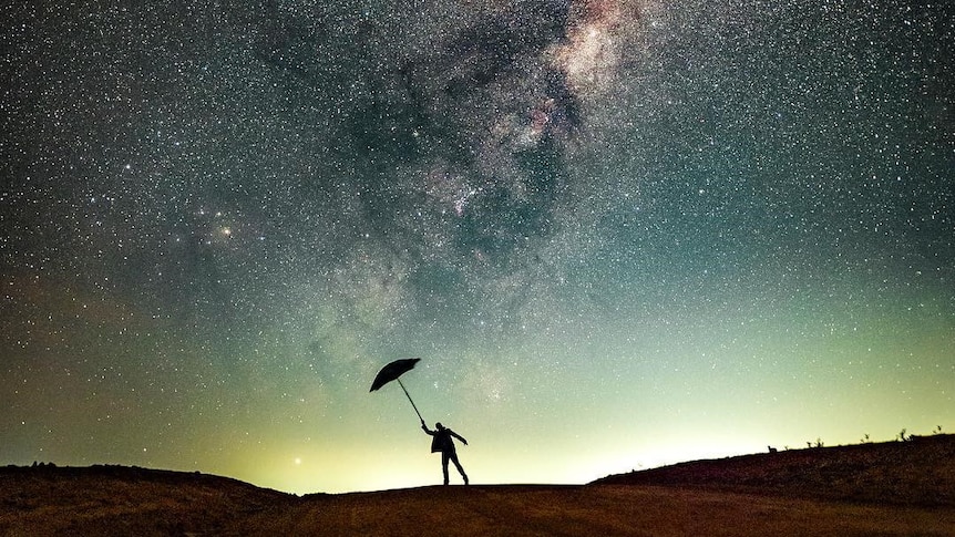 A silhouette of a person with an umbrella against a background of the starry night sky.