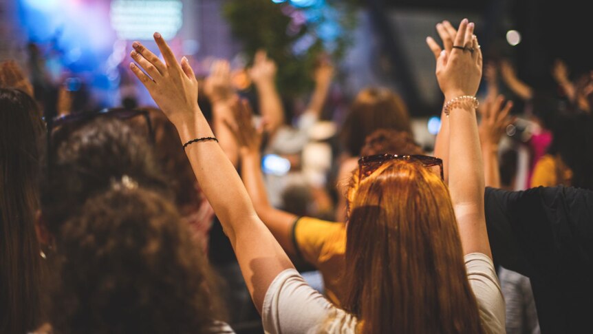 Members of a Christian congregation are shown from behind raising their arms.