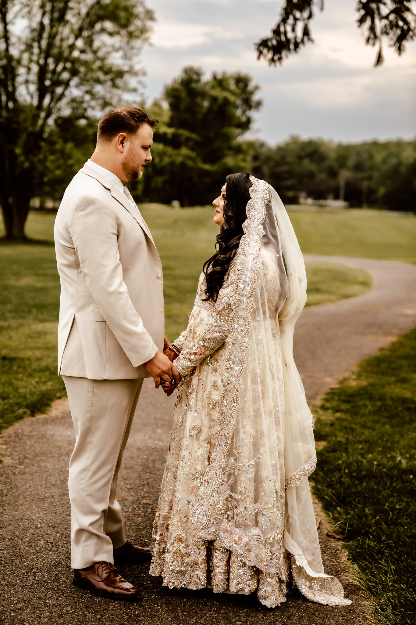 A bride and groom in a park holding hands and facing each other