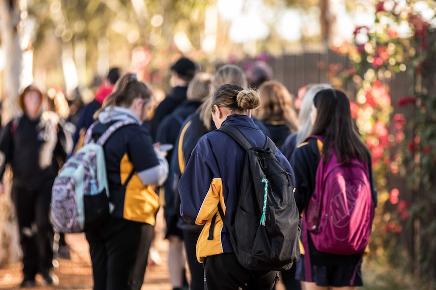 Children wearing backpacks leaving school.