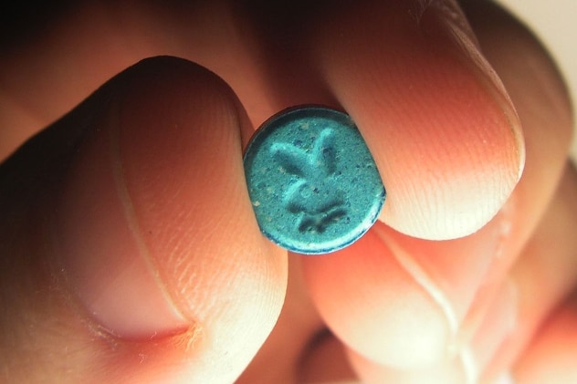 A person holds a tablet containing MDMA in their fingertips.